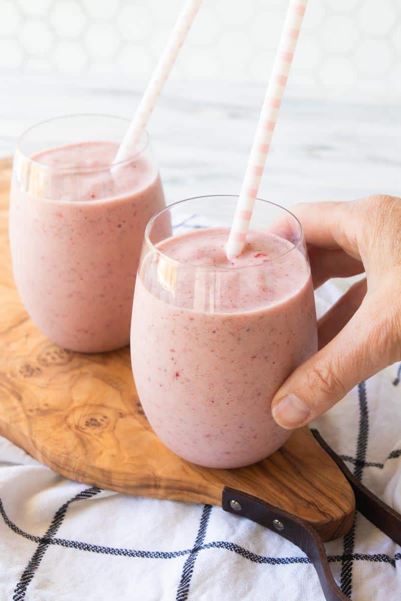 2 protein fruit smoothies in glasses with straws with a hand picking one up