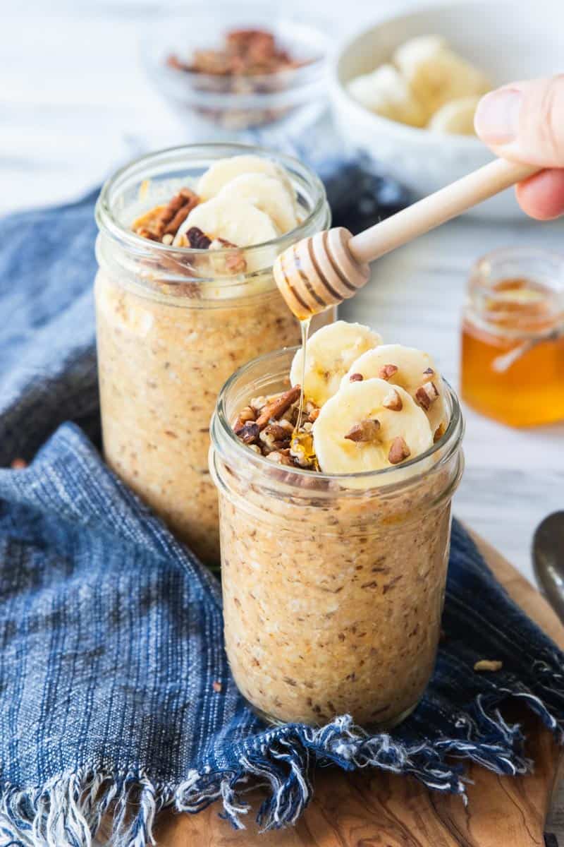 pumpkin overnight oats in a jar with bananas and nuts on top and honey being drizzled