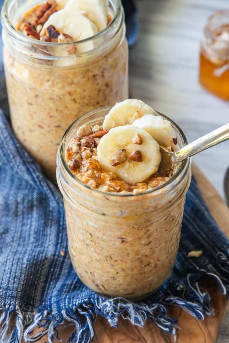 pumpkin overnight oats in a jar with bananas and nuts on top with a spoon