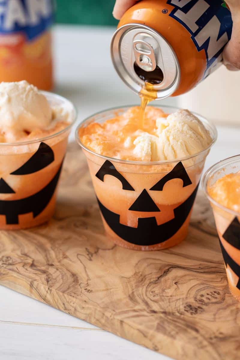 fanta soda being poured onto ice cream in a cup with a halloween jack o lantern face sticker on it