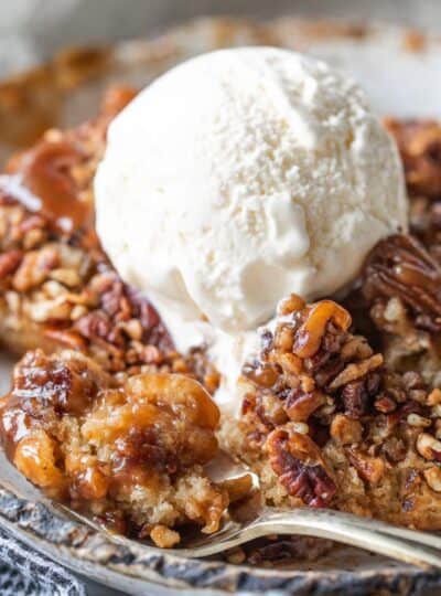 pecan pie cobbler in a bowl with vanilla ice cream on top and a spoon