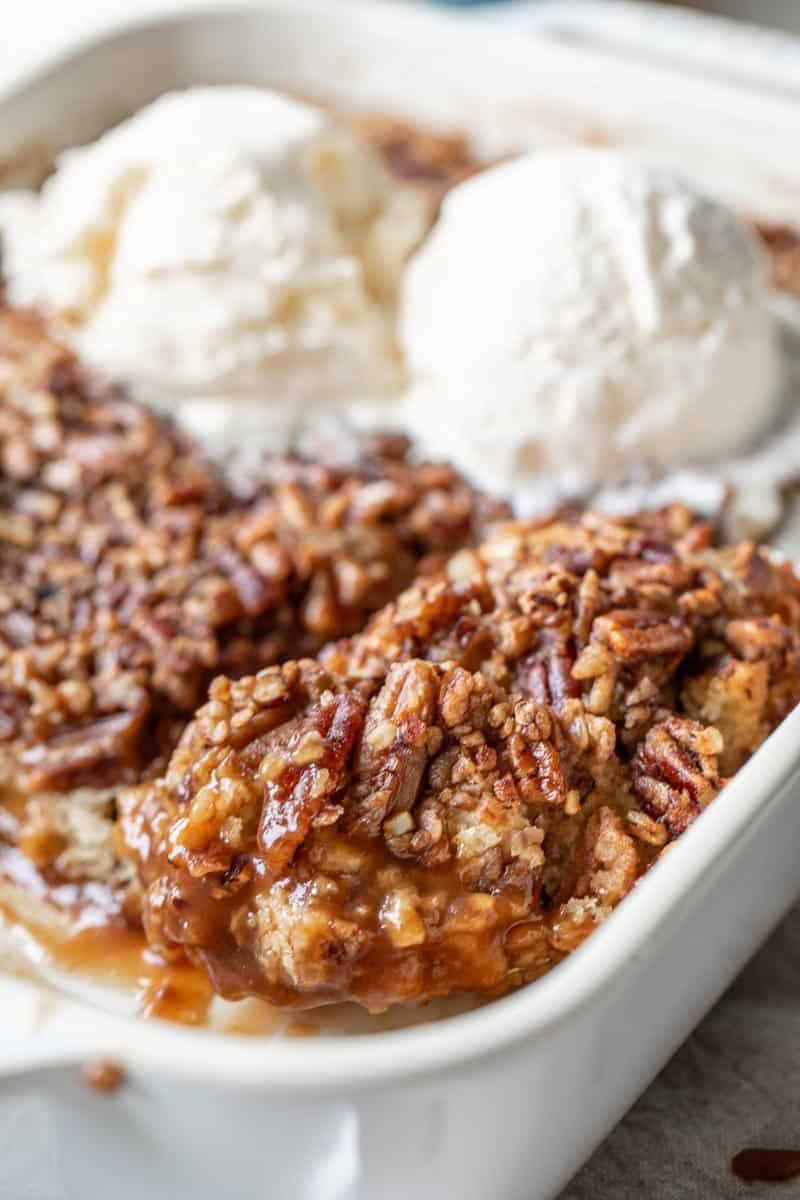 pecan pie cobbler in a baking pan with vanilla ice cream on top