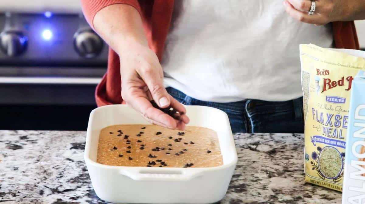 a hand sprinkling chocolate chips on top of baked oatmeal