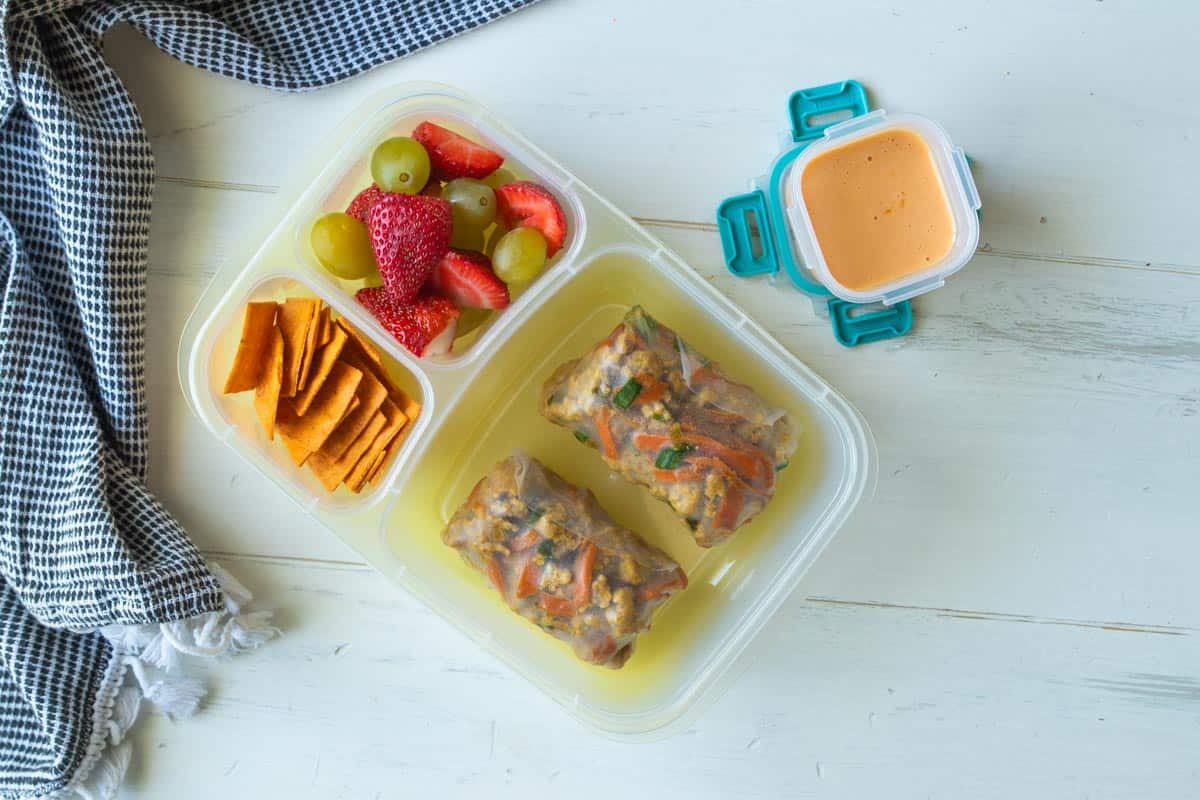 chicken spring rolls in a bento box with cheese crackers, fresh fruit and dipping sauce