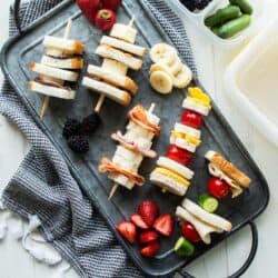 top down view of sandwich skewers surrounded by fresh fruit on a platter