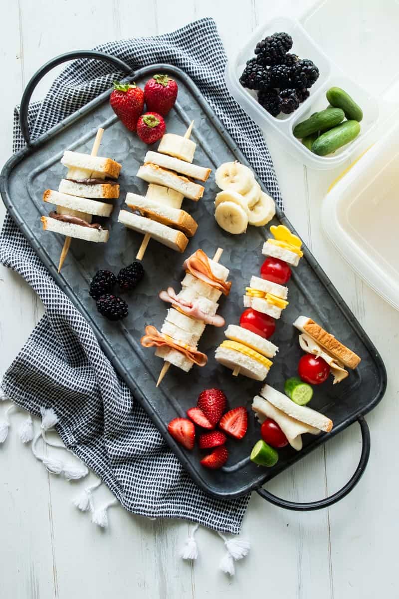 top down view of sandwich skewers surrounded by fresh fruit on a platter