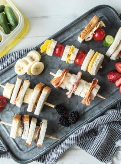 top down view of sandwich skewers surrounded by fresh fruit on a platter