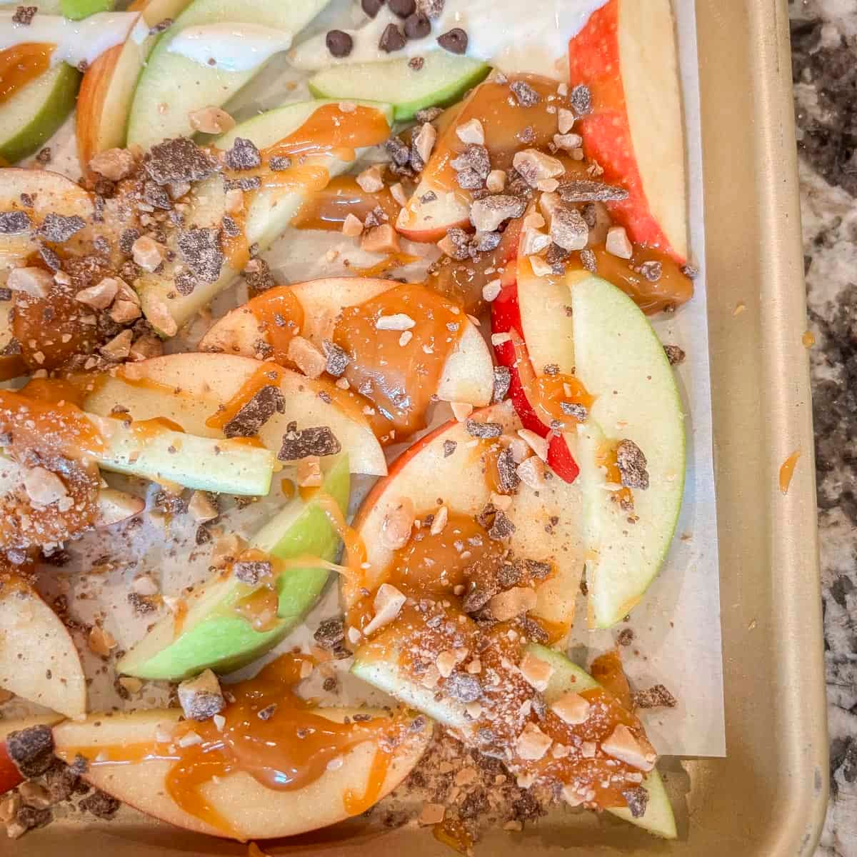 apple slices with caramel and toffee bits on a baking tray